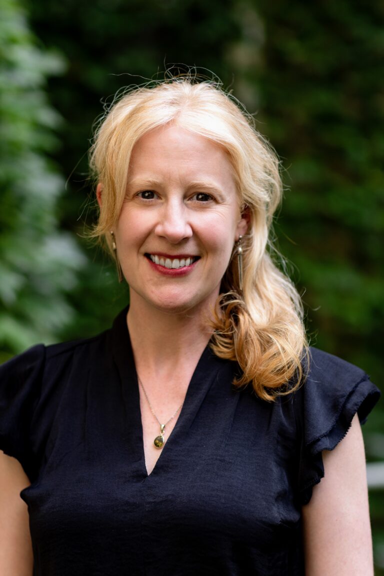 Molly Reinhard Headshot; a woman with blonde hair in a black top smiling at the camera.