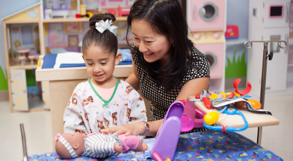 A Child Life Specialist supports a smiling child in a colorful room